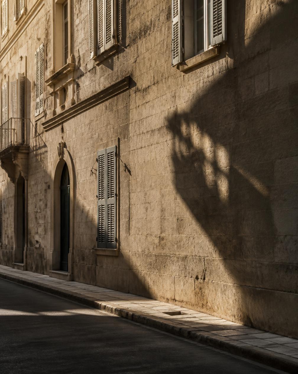 Sunlit stone facade with shutters on a quiet European street